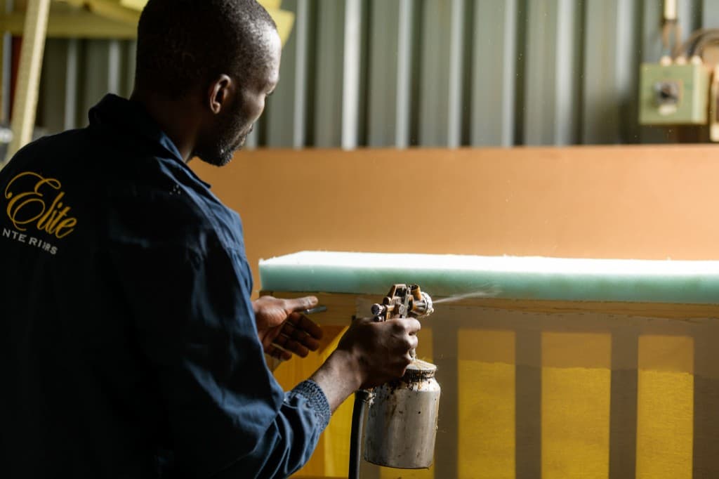 Spray finishing on a frame — branded Elite Interiors workwear visible.